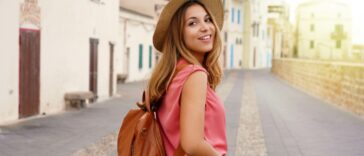 Young stylish tourist woman walking down a Spanish city street while looking back at the camera and smiling