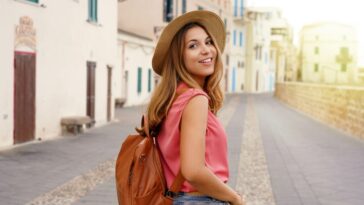 Young stylish tourist woman walking down a Spanish city street while looking back at the camera and smiling